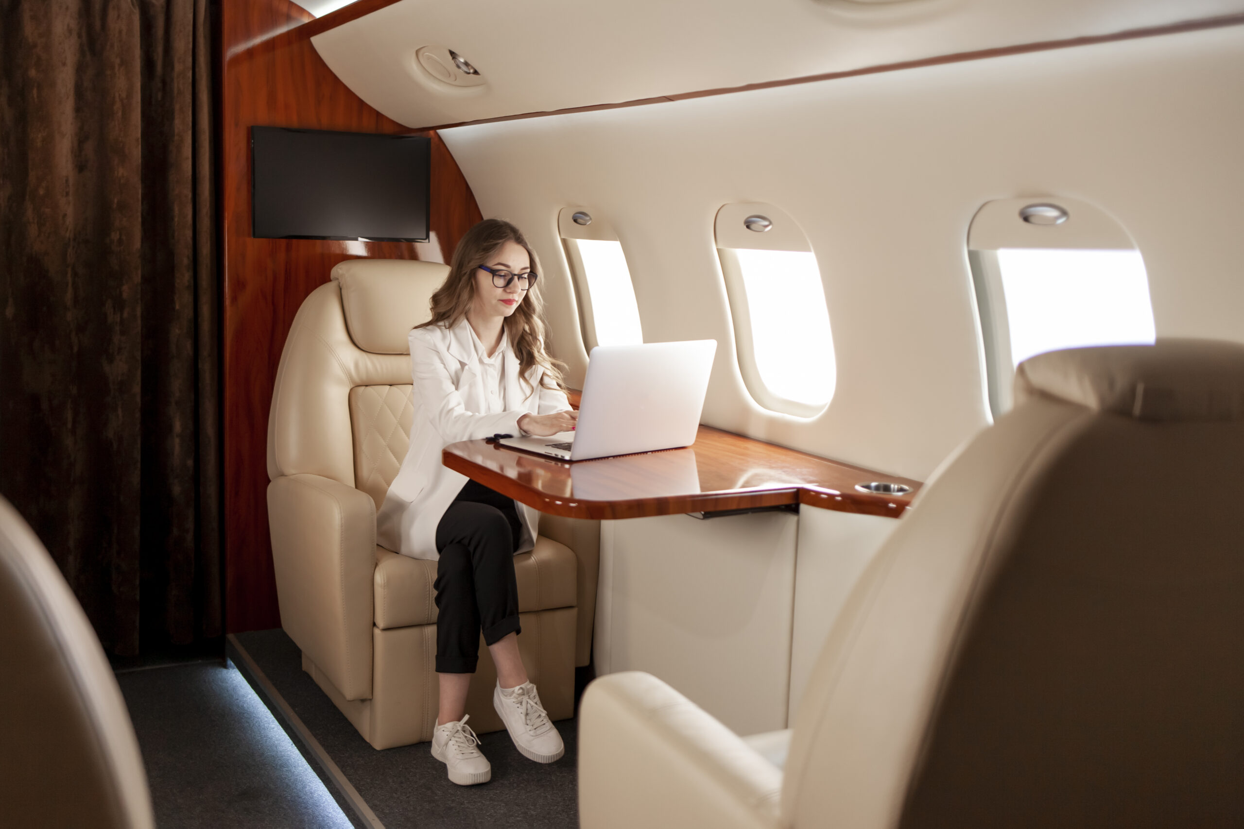 business woman suit glasses flies private luxury jet works laptop scaled - Excel Jet